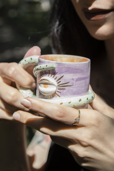 a gril holding purple colour mug. there is an eye on it and its holder snake figure and wrapping around the cup