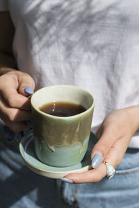 woman holding a green and turquoise coloured cup with its plate