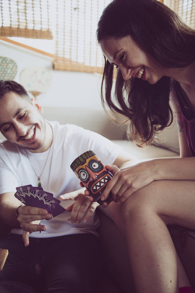 woman holding colourful tiki beer mug. tiki face has two big circle eyes, triangle shaped seven teeth, big orange coloured nose